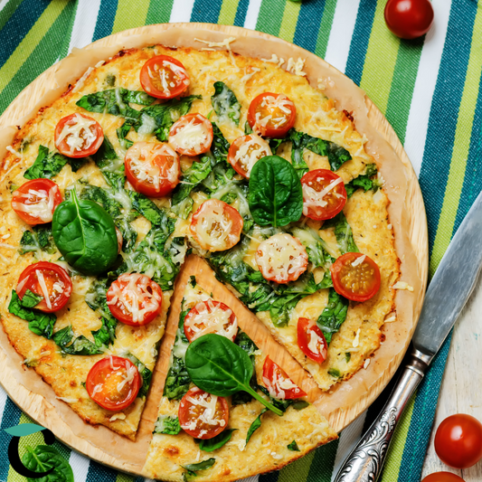 Nahaufnahme von Caulito vegetarischem Low-Carb Blumenkohl-Pizzaboden mit Tomate, Käse und Spinat auf einem Pizzabrett.
